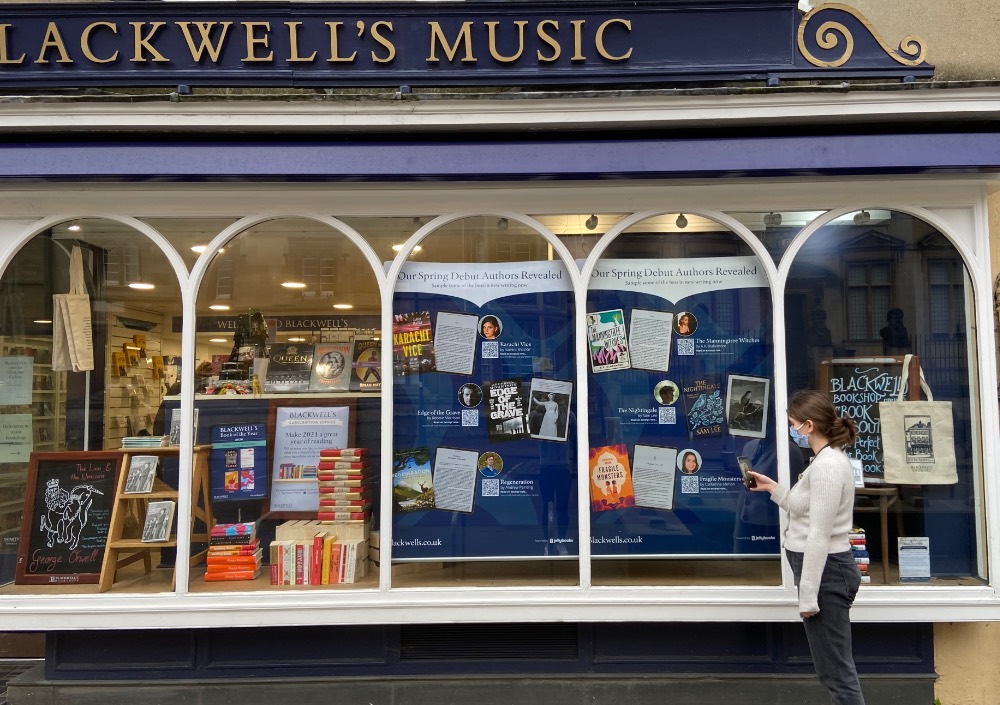 Photo of Blackwell’s shop window showing large poster of new releases containing QR codes to open samples of books.